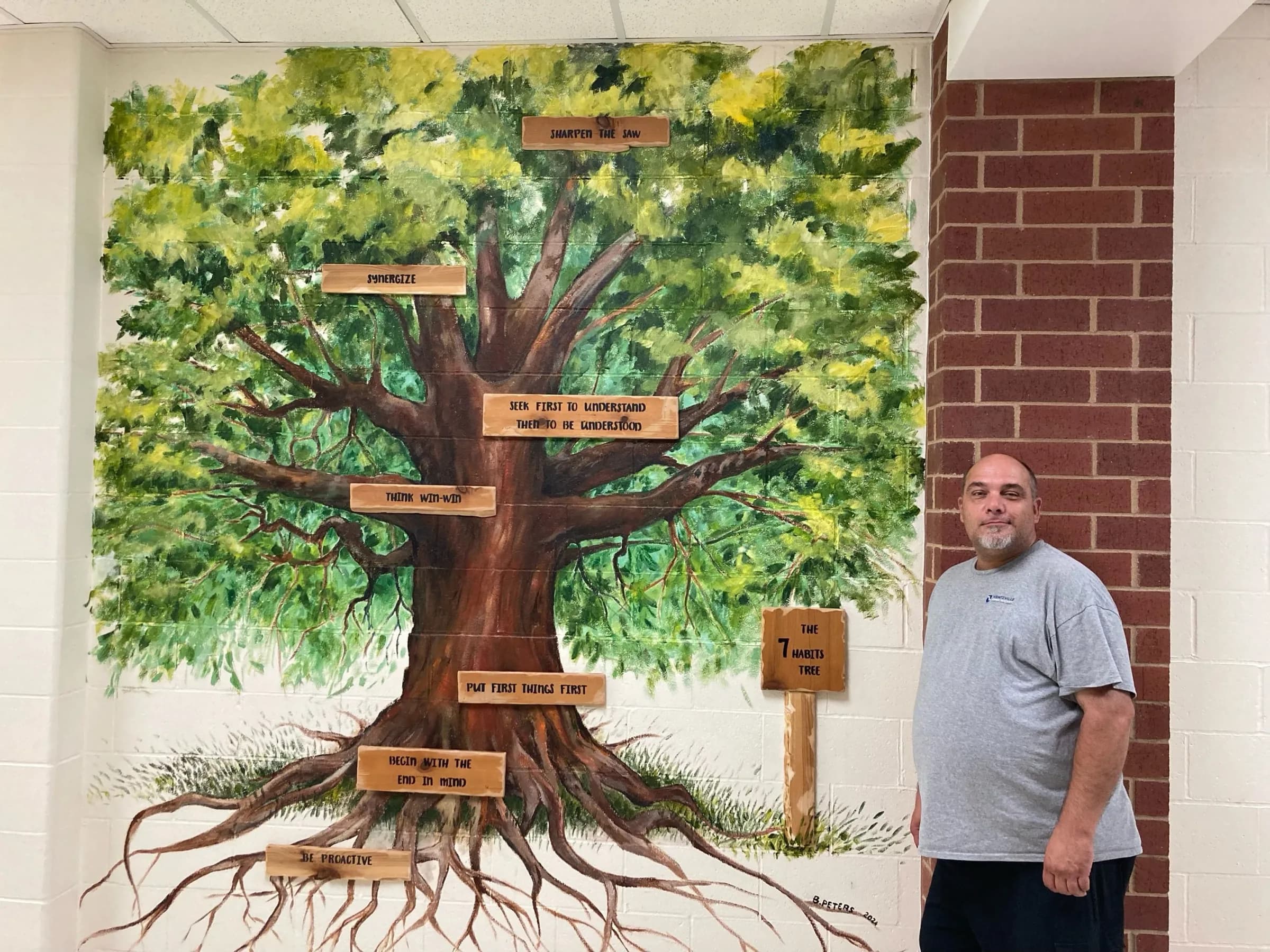 Bryan Peters standing beside his painted Seven Habits Tree mural